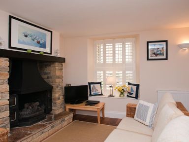 A living room with a stone fireplace a TV on a wooden table cushions on a sofa and a window with shutters at Courtyard House in Dartmouth