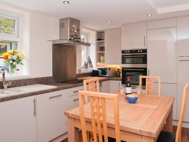 A kitchen with wooden dining table and chairs a bottle of wine and glasses on the table at Courtyard House in Dartmouth