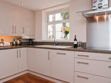 A kitchen with white cabinets a window a bottle of wine two glasses and a bouquet of flowers at Courtyard House in Dartmouth