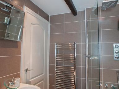 A bathroom with a white door a heated towel rail a glass shower screen and a mirror cupboard at Courtyard House in Dartmouth