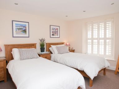 A bedroom with two single beds wooden headboards bedside tables paintings on the wall and a window with shutters at Courtyard House in Dartmouth