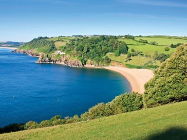 A coastal landscape with a sandy beach surrounded by green hills and trees at Courtyard House in Dartmouth