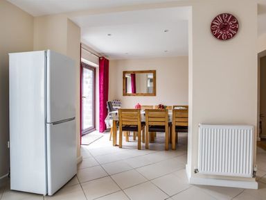 A dining area with wooden chairs around a table a white refrigerator a red clock on the wall and a radiator at New Boathouse Weymouth