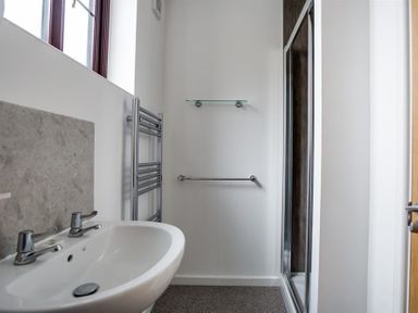 A bathroom with a sink a heated towel rail a glass shelf a towel bar and a shower at New Boathouse in Weymouth