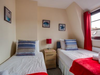 A bedroom with two single beds with striped pillows a bedside table with a lamp and red curtains at New Boathouse in Weymouth