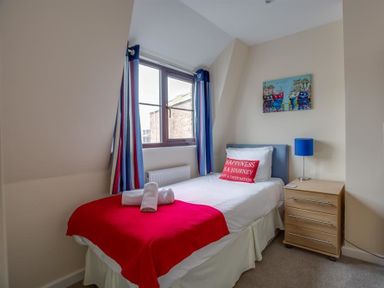 A bedroom with a bed with red and white bedding and a bedside table with a blue lamp at New Boathouse in Weymouth