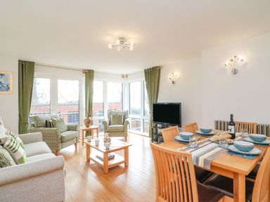 A living room with armchairs a dining table with tableware and a television at Newton's Cove View in Weymouth