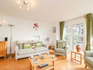 A living room with sofa armchairs coffee table and large glass doors at Newton's Cove View in Weymouth