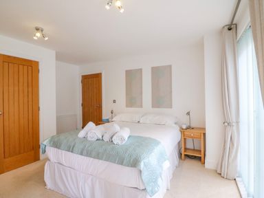 A bedroom with a double bed and rolled towels on it two wooden doors bedside tables with lamps and a window with curtains at Newton's Cove View in Weymouth