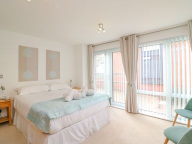 A bedroom with a double bed with rolled towels and two chairs near large windows at Newton's Cove View in Weymouth