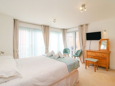 A bedroom with a bed towels on it two chairs a wooden dresser with a mirror and a TV on the wall at Newton's Cove View in Weymouth