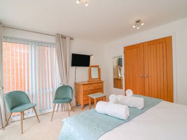 A bedroom with a bed with rolled towels a dresser with a mirror two green chairs vertical blinds and wooden closet doors at Newton's Cove View in Weymouth