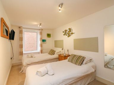 A bedroom with two single beds bedside table wall mirror and window at Newton's Cove View in Weymouth