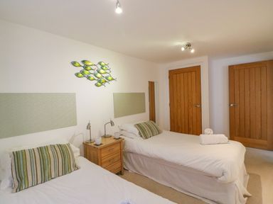 A bedroom with two single beds a wooden nightstand and two wooden doors at Newton's Cove View in Weymouth