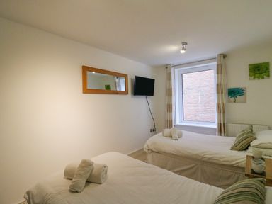 A bedroom with two single beds each with rolled towels a wall-mounted mirror a television and a window with curtains at Newton's Cove View in Weymouth