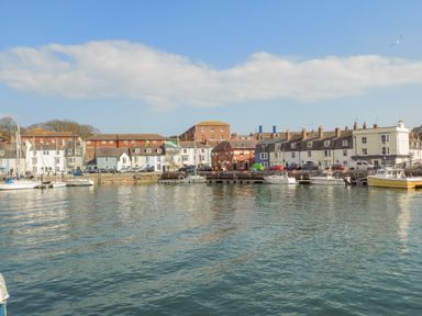 A harbor with boats docked along the waterfront and buildings in the background at Newton's Cove View in Weymouth