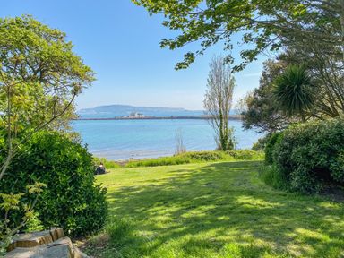 A grassy area with trees overlooking a body of water and distant land at Newton's Cove View in Weymouth