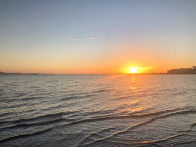A sunset over the ocean with gentle waves and distant land on the horizon at Newton's Cove View in Weymouth