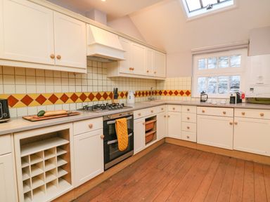 A kitchen with white cabinets a gas stove and oven a window and wooden floor at The Oast House in Brewers Quay Harbour