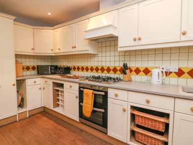 A kitchen with white cabinets a gas stove a kettle knives and baskets at The Oast House in Brewers Quay Harbour