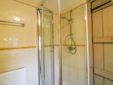 A shower with tiled walls a glass door a wooden door and a radiator at The Oast House in Brewers Quay Harbour