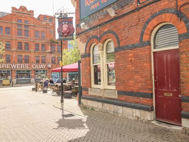 An outdoor seating area with people sitting at tables outside a red brick building with a sign for The Red Lion at Brewers Quay Harbour