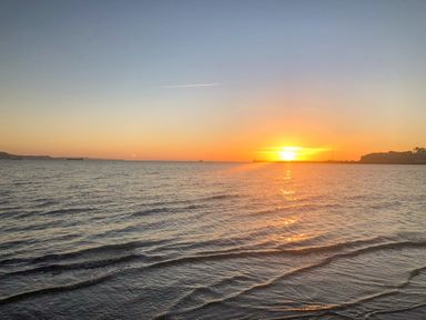 A sunset over the ocean with gentle waves and a coastline at The Oast House in Brewers Quay Harbour