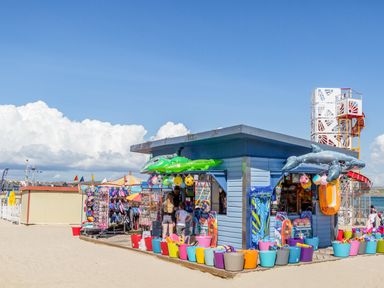 A beachside shop selling inflatable toys buckets and flip flops with people browsing at The Oast House in Brewers Quay Harbour