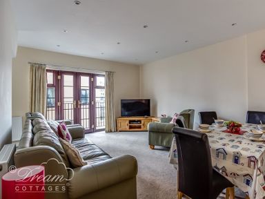 A living room with leather sofas a dining table set with bowls and fruit a television on a wooden stand and double doors with curtains at Old Boathouse in Weymouth