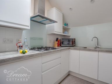 A kitchen with a gas stove, microwave, sink, and white cabinets at Old Boathouse in Weymouth