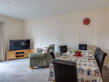 A living room with a TV on a wooden stand a green armchair a dining table with chairs and tableware at Old Boathouse Weymouth