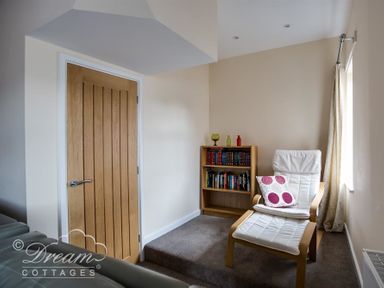 A small reading nook with a wooden door a bookshelf and a white armchair with a footstool at Old Boathouse in Weymouth