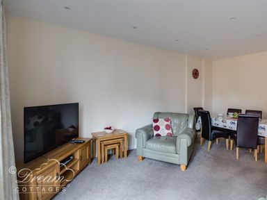 A living room with a television on a wooden stand an armchair with a cushion nested tables and a dining table with chairs at Old Boathouse in Weymouth