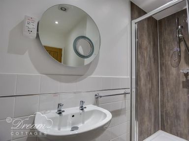 A bathroom with a round mirror above a sink and a shower with wooden style walls at Old Boathouse in Weymouth