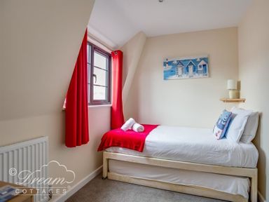 A bedroom with a single bed next to a window with red curtains at Old Boathouse in Weymouth