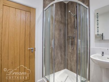 A bathroom with a wooden door a glass shower enclosure and a white sink at The Old Boathouse in Weymouth