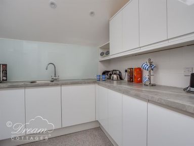 A kitchen with white cabinets a grey countertop a sink a microwave toaster kettle striped mugs and cereal boxes at Old Boathouse in Weymouth