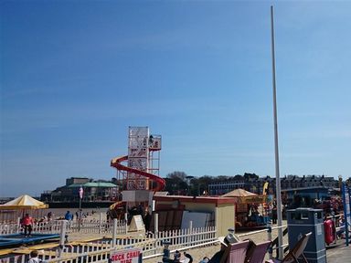 A beach with amusement rides and booths and a sign for deck chair hire at Old Boathouse in Weymouth