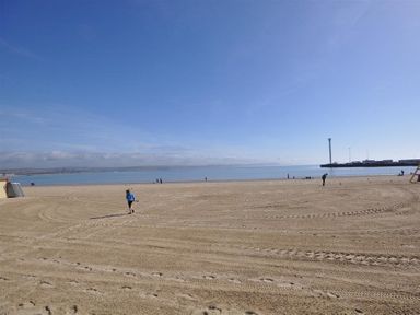A sandy beach with footprints and tire tracks and people walking near the water at Old Boathouse in Weymouth
