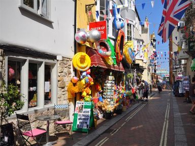 A narrow street with a shop selling inflatable toys and beach items people walking and colorful bunting above at Old Boathouse Weymouth