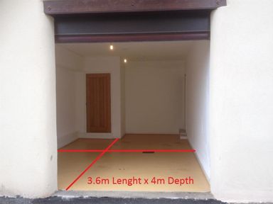 An empty garage with a wooden door at the back and red lines on the floor indicating 3.6m length by 4m depth at the Old Boathouse in Weymouth
