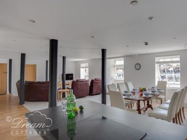 A dining area with a table set for eight and a living room with sofas and a TV at Old Coastguard Apartment 2 in Weymouth