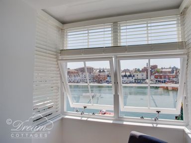 A window with white blinds overlooking a waterfront with buildings at Old Coastguard Apartment 2 in Weymouth