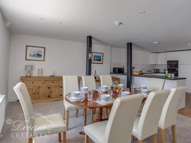 A dining area with a wooden table set for eight and white chairs next to a kitchen with white cabinets and black countertops at Old Coastguard Apartment 2 Weymouth
