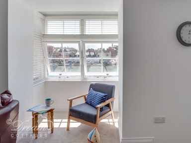A small seating area with a chair and side table next to windows overlooking a harbor at Old Coastguard Apartment 2 Weymouth