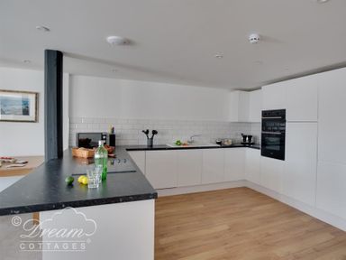 A kitchen with white cabinets black countertops and wooden floor at Old Coastguard Apartment 2 in Weymouth