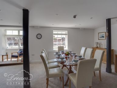 A dining room with a table set for eight and a seating area near windows at Old Coastguard Apartment 2 in Weymouth