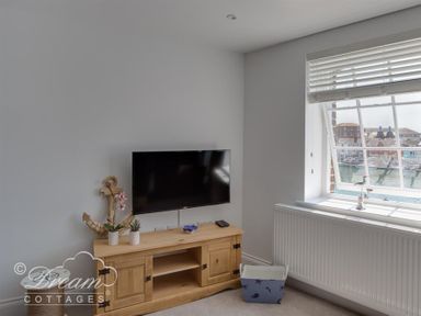 A room with a wall-mounted TV above a wooden cabinet and a window with blinds showing a harbor view at Old Coastguard Apartment 2 in Weymouth