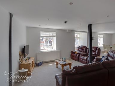 A living room with brown leather sofas a wooden coffee table a wall-mounted TV and windows at Old Coastguard Apartment 2 Weymouth
