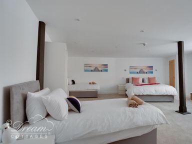 A bedroom with three beds pillows and towels on each bed a bedside table between two beds and artwork on the wall at Old Coastguard Apartment 2 in Weymouth